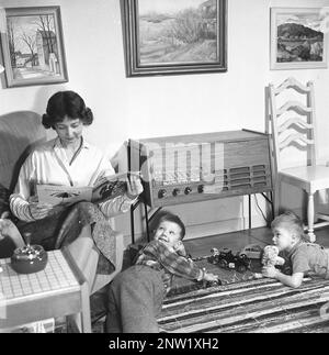 A housewife and mother with her two boys in front of the radio. Typical radio gramophone from 1957. A radio gramophone that gave the opportunity to listen to the radio and play gramophone records in the same unit. Sweden 1957. ref BV19-12 Stock Photo