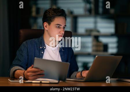 Focused young man employee working at office in evening Stock Photo