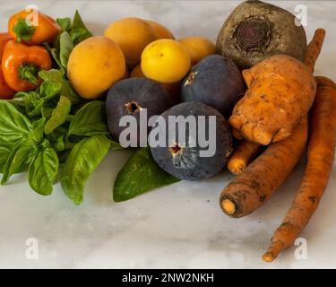 Close-up on organic vegetables and  fruit, against white marble background, viwed from dinner angle, close, showing detail and texture Stock Photo