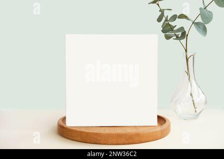 Blank Greeting Card, Invitation Mockup. Front view Eucalyptus Plant, Modern Wooden Plate, Boho Paper Mock Up on Green Table Copy Space. Minimal Busine Stock Photo