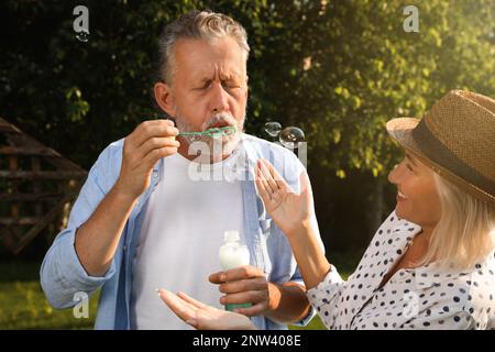 Lovely mature couple spending time together in park. Man blowing soap bubbles Stock Photo