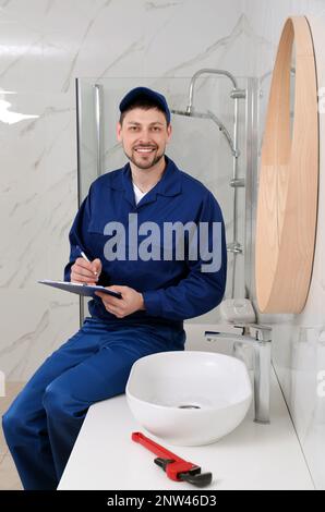 Professional plumber with clipboard checking water tap in bathroom Stock Photo