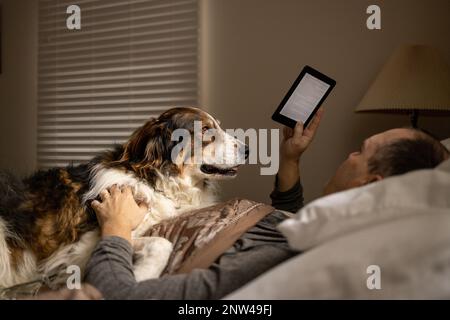A man and his shepherd dog lying in bed and relaxing in a bedroom. Stock Photo