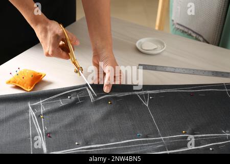 Seamstress cutting fabric following chalked sewing pattern at table in workshop, closeup Stock Photo