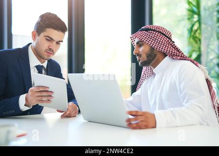 Complimentary skill sets for a successful collaboration. Shot of a young muslim businessman using a laptop and digital tablet with his colleague at Stock Photo