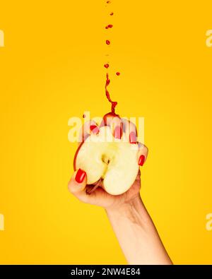 Closeup female hand with red painted nails squeezing half of apple fruit over yellow background. Contemporary art. Drops of juice fly up Stock Photo