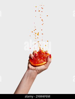 Female hand with bright manicure squeezes half of grapefruit. Pop art food photography. Drops of juice fly up Stock Photo