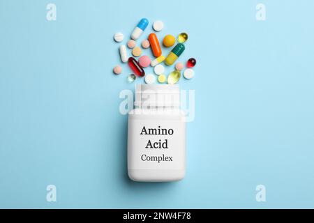 Plastic bottle with Amino Acid Complex and pills on light blue background, flat lay Stock Photo