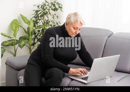 Front view concentrated pleasant mature older woman looking at computer screen. Happy middle aged lady web surfing information, ordering food online Stock Photo