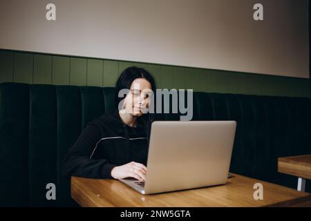 Attractive female freelancer chatting with her friends while sitting front open computer in vintage coffee shop Stock Photo