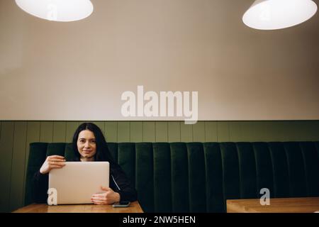 Attractive female freelancer chatting with her friends while sitting front open computer in vintage coffee shop Stock Photo