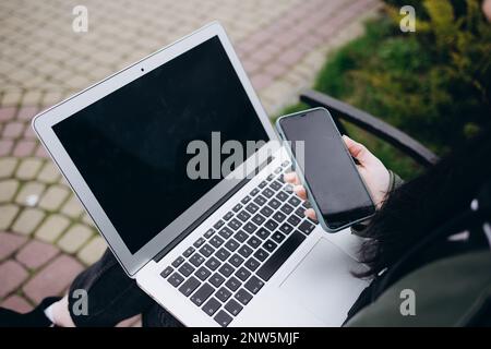 Close-up of female hands typing text on on laptop with blank black monitor screen with copy space for promotion on the urban background. Business conc Stock Photo