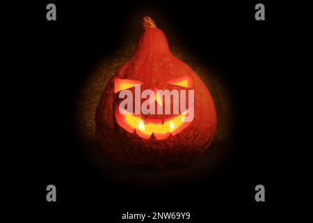 Close-up on a Jack O' Lantern lit in the dark and reflecting on a black surface in front of it. Stock Photo