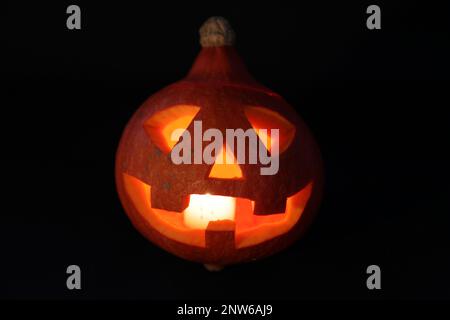 Close-up on a Jack O' Lantern lit in the dark and reflecting on a black surface in front of it. Stock Photo