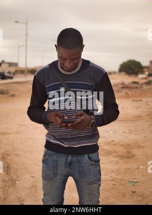 A young african male with his smartphone in the street, Nouakchott Stock Photo