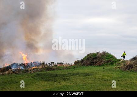 Ballylickey, West Cork, Ireland. 28th Feb, 2023. A Ballylickey farmer watches over a fire he set in order to burn gorse and vegetation. From tomorrow, it is illegal to burn vegetation until the 1st September. The burning of vegetation is controlled by the Wildlife Acts. Credit: AG News/Alamy Live News Stock Photo
