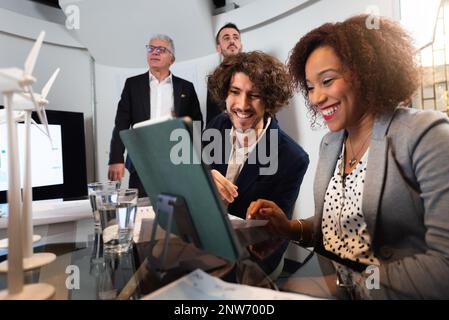 Happy teamwork planning a new project of renewable energy. Multiracial business people using computer working in office. Stock Photo