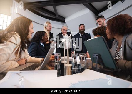 Group of multiracial business people sitting at desk in office discussing about new project of renewable energy. Sustainability concept. Stock Photo