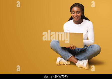 Modern woman using laptop computer isolated on yellow. Portrait of multiracial female using online technology for doing business, computer app for accounting Stock Photo