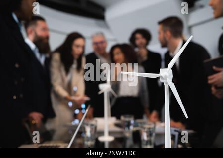 Close-up model of wind turbine. Defocused large group of engineers working on new project. Stock Photo