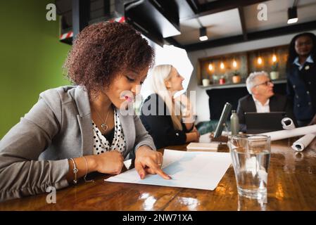 Close-up latin young businesswoman or student sitting at desk analyzing data. Team work at background. Stock Photo