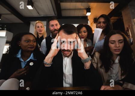 Close-up young businessman stressed because overworked. Male sitting at desk with colleague putting pressure. Stock Photo