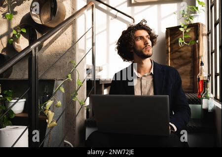 close-up young hipster man sitting in stairs looking out window with serious pensive face illuminated by natural lighting. Creative programmer or free Stock Photo