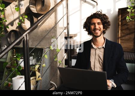 Hipster student posing at camera smiling. Guy sitting on a stair in a lounge and using computer laptop Stock Photo