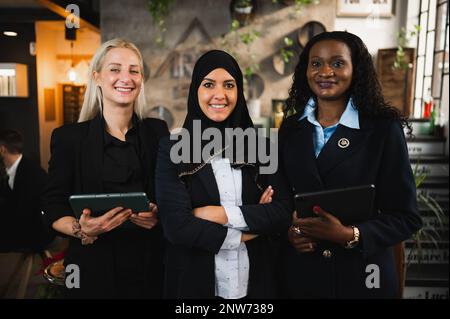 Three young elegant business women with diverse ethnicity standing posing at camera smiling. Stock Photo