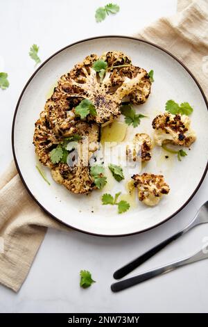 Baked cauliflower steak on white plate with cilantro leaves Stock Photo
