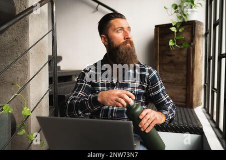 Hipster man looking out window.Guy sitting on stairs using computer. Stock Photo