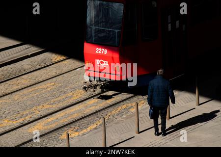 Belgrade, Serbia - February 23, 2023: One man with briefcase standing alone at bus stop and a tram passing by in front of him in motion blur, high ang Stock Photo