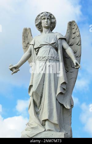 Weathered early twentieth century statue of Arch-angel Michael in art deco style with broken sword in New York cemetery. Scattered white clouds and bl Stock Photo