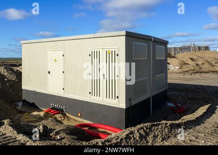 New modern electric transformer room building with grey doors and yellow hazard signs on blue sky background in a new unfinished industrial facility Stock Photo