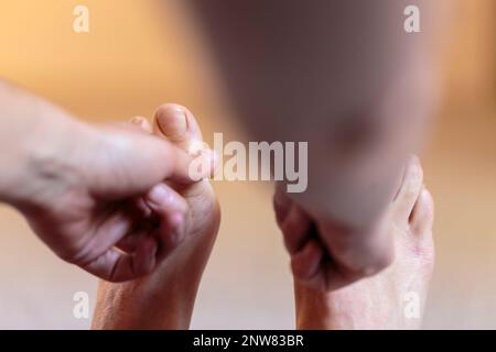 Yogini doing forward bending exercise on the floor, reaching foot and locking index finger and thumb on yogi toe lock with both hands Stock Photo
