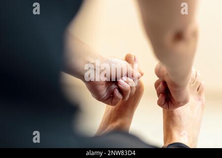 Yogini doing forward bending exercise on the floor, reaching foot and locking index finger and thumb on yogi toe lock with both hands Stock Photo