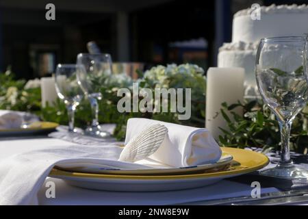 Elegant table setting decorated with green leaves boho-inspired centerpiece, shells and white linen cloth for a engagement party, wedding reception or Stock Photo