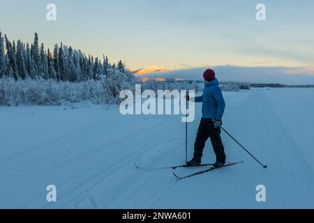 Amazing pastel sunset views along the Yukon River with one person skiing in distance with beautiful winter scenery. Stock Photo