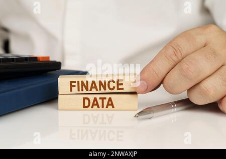 Business concept. In the hands of a businessman, wooden blocks with the inscription - FINANCE DATA, next to a notebook and a calculator. Stock Photo