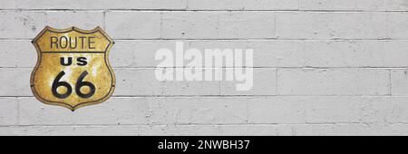Panoramic photo of a brick wall painted in white with on its left side, a rusty route US 66 sign. Stock Photo