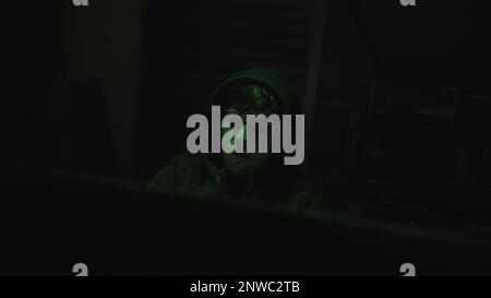 Handsome Hooded Young Computer Hacker or Programmer Working on Computer with Green Lights in Background Stock Photo