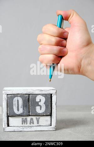May 3 on calendar, hand holding green ballpoint pen gray background.Concept for Press Freedom Day Stock Photo