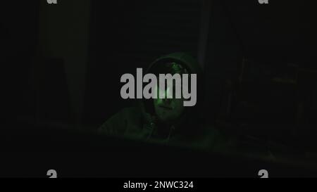 Hooded Young Computer Hacker or Programmer Working on Computer with Green Lights in Background Stock Photo