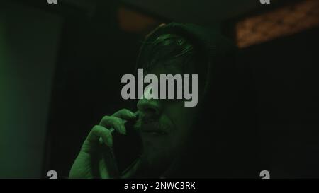Mysterious hacker or programmer in a green-lit room talking on the phone Stock Photo