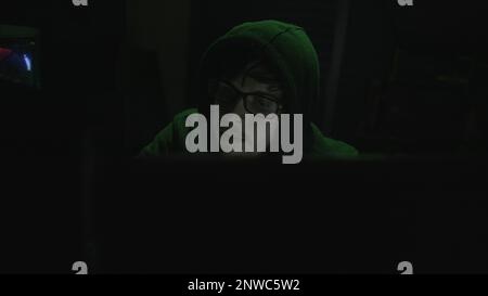 Young Programmer in Hoodie and Black Glasses Immersed in Coding with Green Illumination Stock Photo
