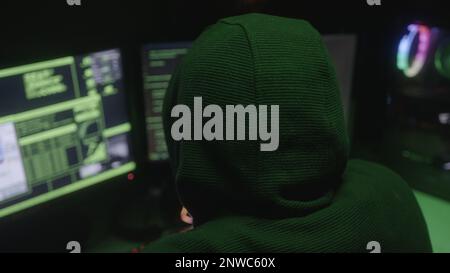 Young male hacker or programmer in hoodie hacking at computer with his back turned Stock Photo