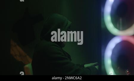 Programmer or hacker working on desktop computer with green lights in side view Stock Photo