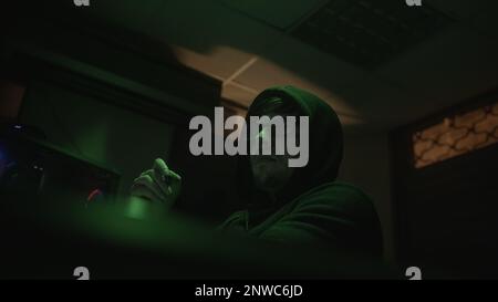Analysing with a Pen, Hooded Computer Hacker or Programmer in Glasses Working at the Computer Stock Photo