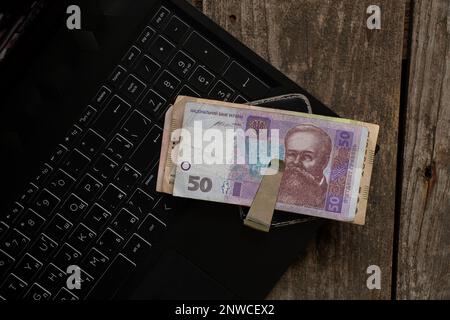 Ukrainian 50 UAH money in a money clip lie on a laptop on the table, finances and work Stock Photo