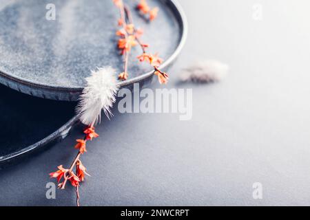 Handmade round ceramic plates decorated with spring branches and feathers. Close up of lacquered blue vintage dishes on grey background. Stylish moder Stock Photo